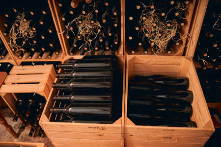 Wine cellar or storage room with bottles of alcoholic drink in wooden boxes with vintage year...