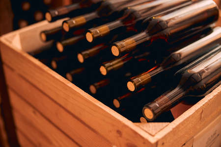 Wooden box with glass bottles of alcoholic drink in wine cellar