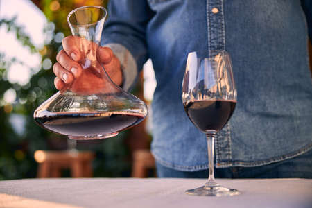 Close up of a glass of red wine on the table. Man standing with a decanter in front of itの写真素材
