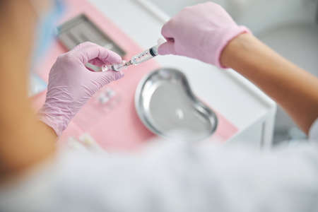 Cropped photo of a cosmetologist withdrawing the medication from an ampule into a plastic syringe