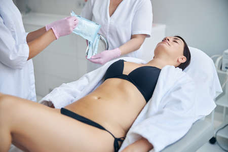 Dark-haired adult woman lying with closed eyes on a cosmetic couch during a medical procedureの写真素材