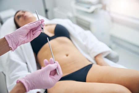 Qualified female dermatologist in latex gloves holding a stainless steel biopsy instrument in her...