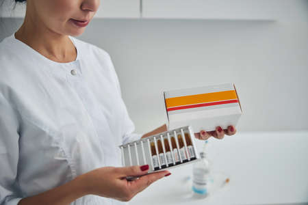 Cropped photo of a Caucasian doctor holding a carton box of ampules in her handsの写真素材