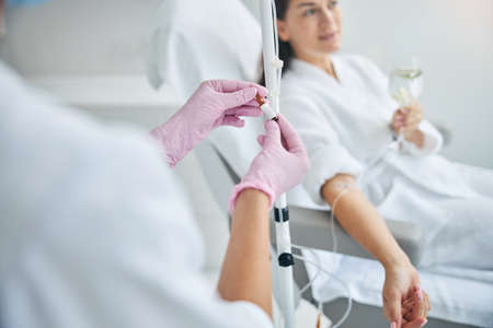Dark-haired spa client with a glass of drink in her hand looking away during the intravenous therapyの写真素材