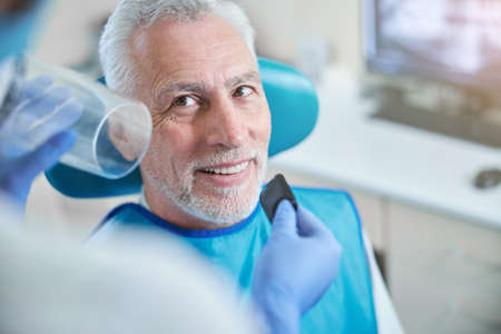 Optimistic elderly citizen sitting down while being prepared for a dental x-ray