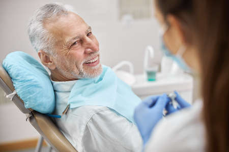 Senior patient of a clinic sitting in a dental chair and watching his dentist start a dental drill