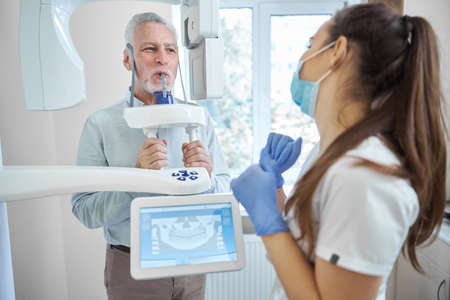 Brunette female dentist wearing a mask looking at an aging man having his teeth x-rayedの写真素材
