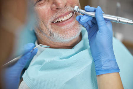 Close-up photo of an elderly man smiling while having his treated with a dental drillの写真素材