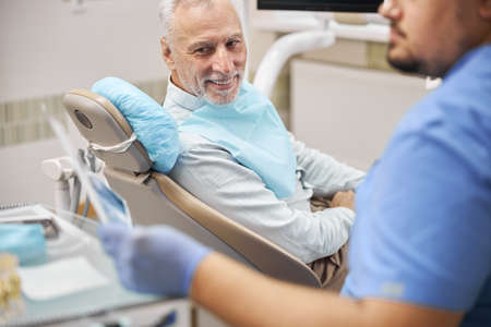 Dental technician wearing blue scrubs showing a dental radiogram to his elderly patient