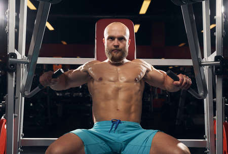 Sweaty shirtless man exercising while sitting on a gym benchの写真素材