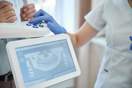 Cropped photo of a dentist pressing buttons on a panoramic x-ray machine while helping her patient get a dental x-rayの写真素材