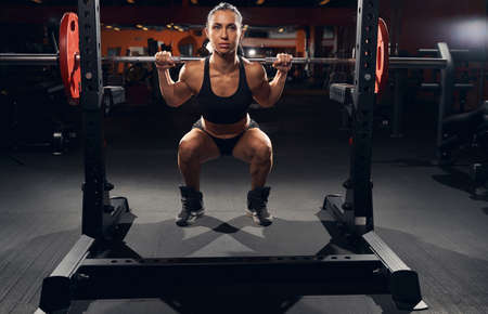 Beautiful muscular woman squatting while holding a barbell with weights on her shouldersの写真素材