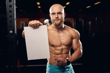 Copy space photo of a fit muscly man wearing no shirt and holding an empty white board