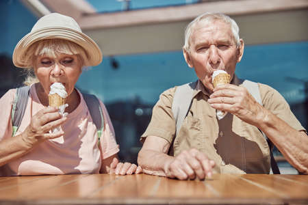 Waist-up portrait of a pensive senior lady and her spouse eating vanilla ice cream outdoorsの写真素材