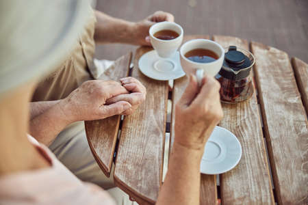 Cropped photo of an aged lady and her spouse holding hands in a street cafe
