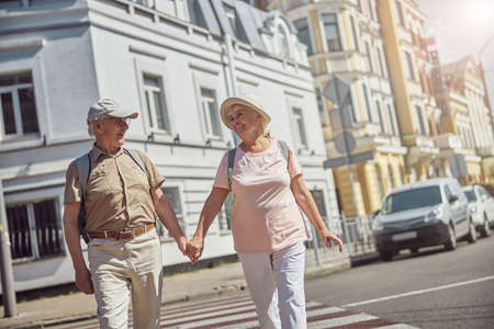Low angle of a happy elderly couple walking hand in hand across the zebra crossingの写真素材