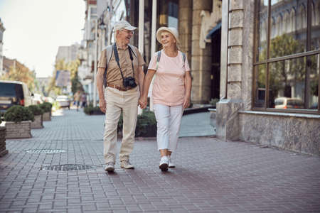 Full-length portrait of joyful aged tourist couple walking hand in hand around the city centerの写真素材