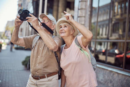 Joyous female tourist in a sunhat pointing at something to her spouse with a digital deviceの写真素材