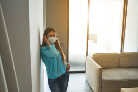 Front view of a serious lady in a protective mask standing in a living room