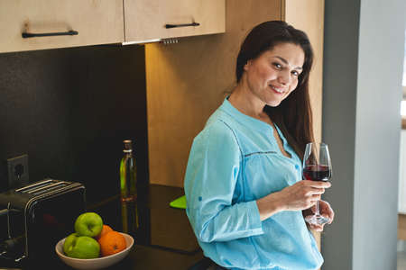 Waist-up portrait of a smiling attractive dark-haired lady with a wineglass posing for the cameraの写真素材