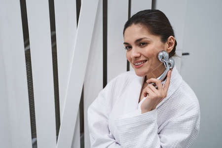 Portrait of a dreamy woman massaging the skin on her face with a 3D massager