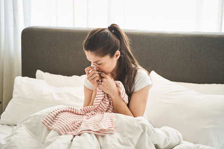 Waist-up portrait of a sad young Caucasian female smelling a polo shirt in her handsの写真素材