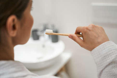 Cropped photo of a young dark-haired Caucasian female cleaning her teeth with a wooden brush