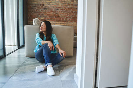 Front view of a woman sitting cross-legged on the tile floor in a living room