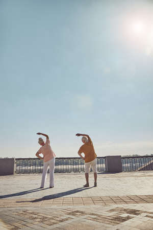 Back view of a gray-haired woman and her husband in casual wear stretching oblique musclesの写真素材