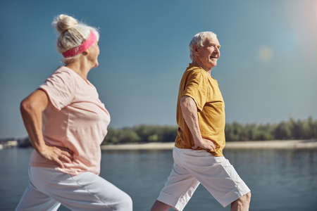 Side view of a smiling senior male yogi and his female partner exercising together outdoorsの写真素材