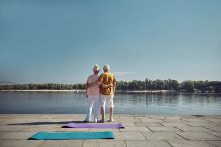 Back view of an elderly couple with their arms around each other waist standing outdoorsの写真素材