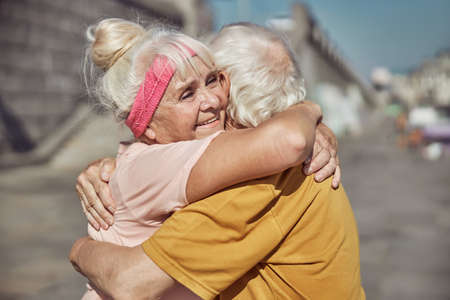 Waist-up portrait of an attractive senior lady with a happy smile hugging a gray-haired man