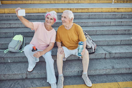 High-spirited attractive senior woman photographing herself and her pleased gray-headed Caucasian...