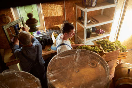 Busy elderly man and his young son preparing materials and equipment for making wine
