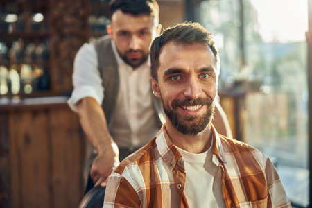 Close-up photo of a joyful man sitting at a barbershop and looking at the camera while having an appointment with his barberの写真素材