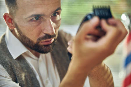 Close-up photo of a responsible barber looking attentively at electric hair trimmer making sure he cleaned it wellの写真素材