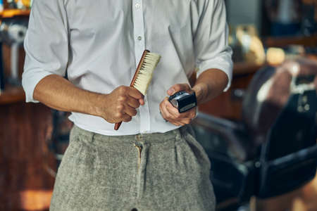 Cropped photo of a well-dressed barber holding a brush and electric hair trimmerの写真素材