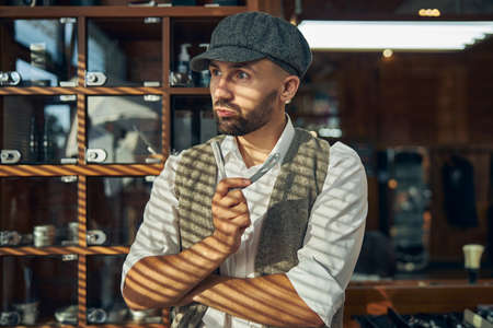 Waist-up photo of a serious hair-stylist holding a cut-throat razor and looking away from the cameraの写真素材