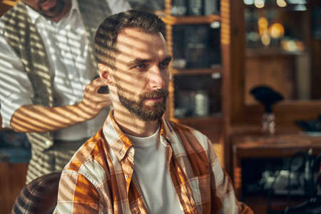 Close-up photo of a bearded young man having an appointment at a stylish barbershopの写真素材
