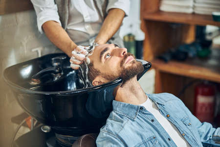 Male customer of a barbershop having his hair shampooed and washed by a skillful hair-stylistの写真素材