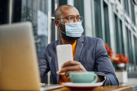 Cheerful Afro-American man wearing mask on his face while working at his business idea on distanceの写真素材