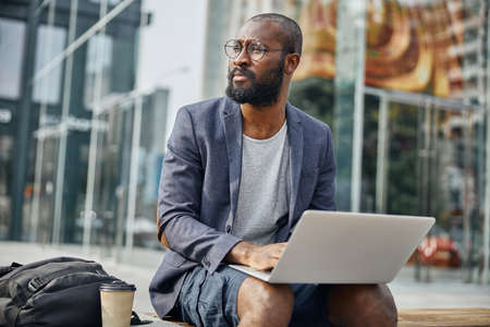 Delighted dark-skinned male siting on the bench and being deep in thoughtsの写真素材