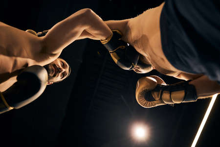 Low-angle shot of two naked sparring partners striking each other with their fists in boxing gloves