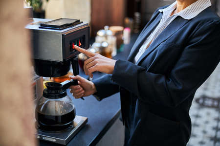Conscious office worker standing in semi position while using coffee-machineの写真素材