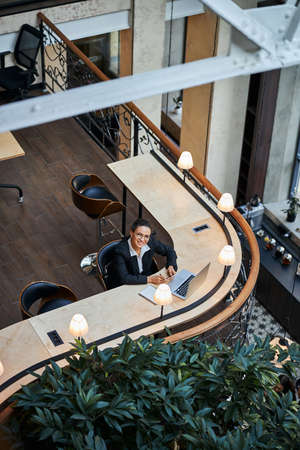 Cheerful international female person sitting in front of her laptop while working with great pleasureの写真素材