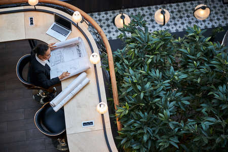 Attentive brunette designer bowing her head while looking at sketch before the meeting
