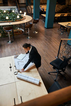 Concentrated brunette woman bowing her head while talking per telephone and looking at sketch