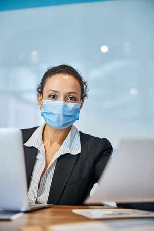 Pleased young woman sitting at her workplace while looking straight at cameraの写真素材