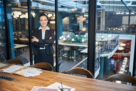 Cheerful international woman keeping smile on her face while crossing arms on chest and looking at...