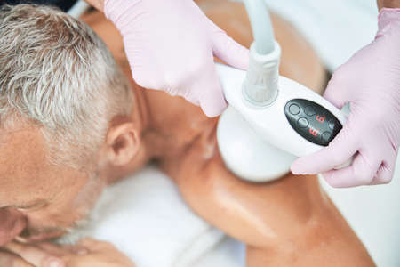 Cropped photo of a relaxed man laying down while having a non-invasive ultrasound cavitation...